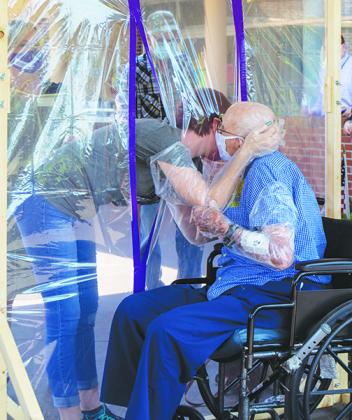 Julie Byers hugs her grandfather, Burcell Donoho, through a plastic protective barrier Friday after not being able to see him for months because of coronavirus precautions.