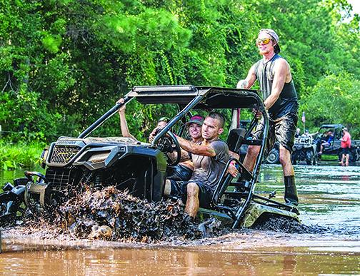 Four people ride a utility-terrain vehicle through the mud on Labor Day weekend this year at Hog Waller.