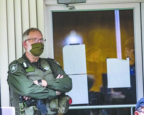 A Putnam County Sheriff’s Office deputy guards the door to City Hall in Crescent City on Thursday as residents who were not allowed inside because of COVID capacity regulations look through the glass doors.
