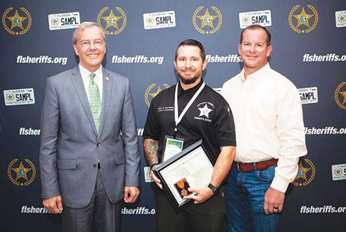 At the Florida Sheriff’s Association Summer Conference on Tuesday, Collier County Sheriff Kevin Rambosk, left, and Putnam County Sheriff Gator DeLoach, right, present Putnam County Sheriff’s Office Maj. Scott Surrency with an award for administering CPR to a woman struck by lightning on a Naples beach the day before.