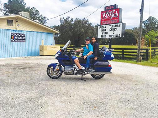 Owners Monique and Bobby Glaize sit on a motorcycle in front of their restaurant, Bobby G’s River Pub.