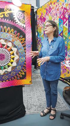  Dannise Kemp, owner of Miss D’s Quilts, stands next to the Best in Show quilt, “On The Spectrum” by Nikki Hill.