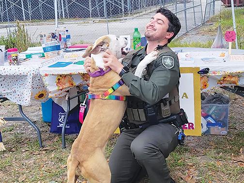A friendly dog from the Putnam County Animal Control Department hugs sheriff’s office Deputy Nick Zagami during an adoption event Saturday. 