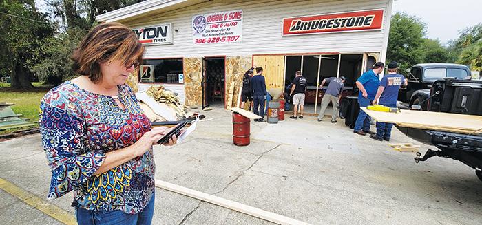 Eugene & Sons Tire & Auto co-owner Leota Wilkinson stands in front of her damaged business as she looks over crash scene pictures on her phone.