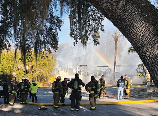 Firefighters stand in front of a burnt building in Welaka after dousing the flames Monday.