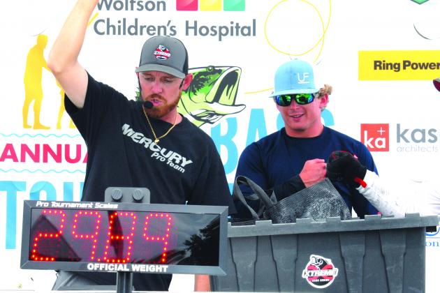 Tournament emcee Brian Stahl raises his fist to announce the winning weight for Austin Black, right, and partner Wyatt Kenney at Saturday’s Wolfson Children’s Hospital Bass Tournament at Palatka Dockside. (GREG WALKER / Daily News correspondent)