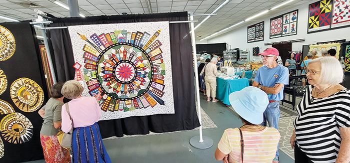 Visitors to the Ninth Annual Quilts by the River quilt show at Ms. D’s Quilts in Palatka inspect and discuss the show’s second-place applique quilt, “Our Community,” on Friday afternoon.