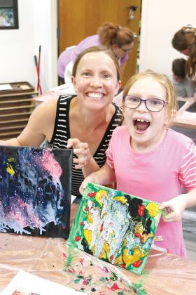 Amanda Doyle, left, and daughter Evelyn Dole, 7, react to their finished Practical Pour Painting projects they created at the Palatka Library.