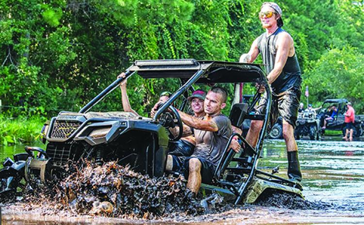 Four people ride a utility-terrain vehicle through the mud on Labor Day weekend this year at Hog Waller.