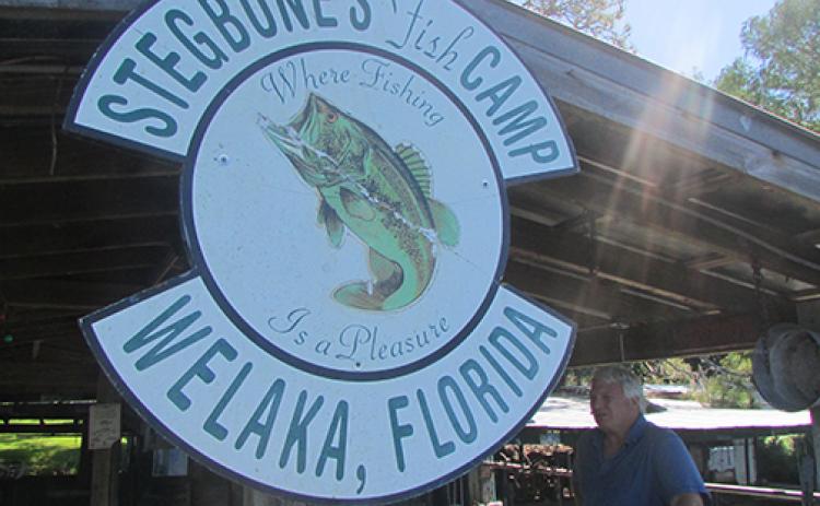 Stegbone's owner Jim Stege talks about the history of the fish camp underneath a Stegbone's sign on the dock.