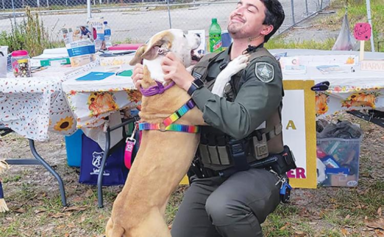 A friendly dog from the Putnam County Animal Control Department hugs sheriff’s office Deputy Nick Zagami during an adoption event Saturday. 