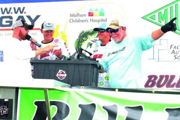 Tournament co-emcee Paul Hamilton makes the hand-raised call of winning weight 28.29 pounds for Parker Stalvey (second, left) and Syler Prince (second, right) at Saturday’s Wolfson Children’s Hospital bass tournament. At left is co-emcee Brian Stahl. (GREG WALKER / Daily News correspondent)
