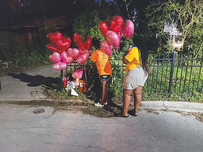 Two mourners tie balloons to a memorial on the gate at 1019 Washington St. in Palatka on Monday, the same day a structure fire caused the deaths of three adults.