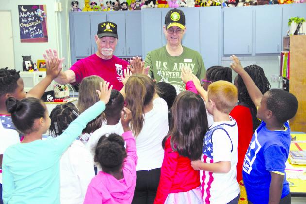 Veterans Lester Sheppard and Sam Wimberly get high-fives from first-grade students at Mellon Elementary School in Palatka on Friday.