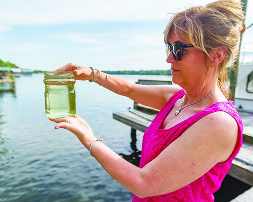 In April 2019, Cathleen Holzknecht holds up a jar of water that was scooped out of the river. Usually, a sample like this would be almost clear, but algae in the water gave it the green tint.