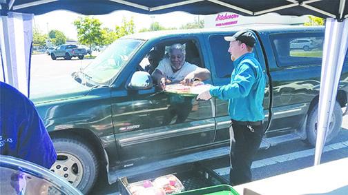 Cody Johnson distributes a meal to a local resident Saturday at Hitchcock’s Market in East Palatka during the store’s event to benefit people affected by COVID-19.