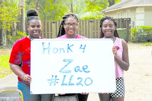 From left, Janessa Purifoy, Lamiya Alridge and Jaylah Rqsher sit by the roadside encouraging passing motorists to show support for their late friend, Xavier Frazier.