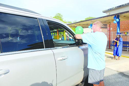 Kelley Smith Elementary School Principal Mike Tucker ties a balloon to a car during Wednesday’s drive-thru graduation ceremony. 