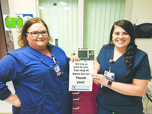 Putnam Community Medical Center’s director of critical care, Callie Nave, and house supervisor Charli McCullough hold a sign thanking residents for staying home during the coronavirus pandemic.