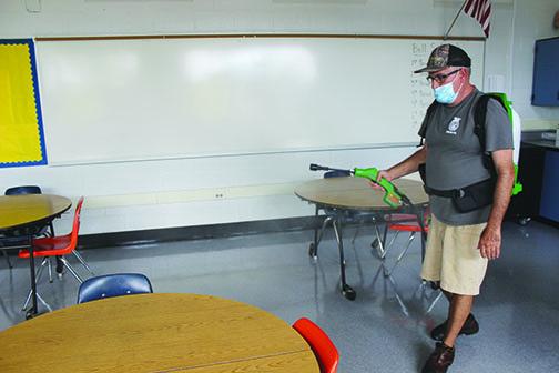 Jenkins Middle School head custodian Tom Willis sprays down a table in a classroom. 