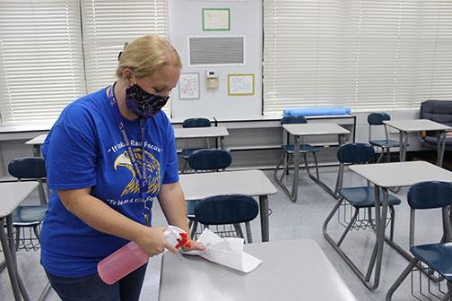 Jenkins Middle School teacher Amanda Pinkerton wipes down a desk Friday in preparation for students returning to class Monday.