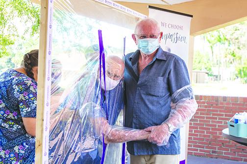 Jim Donoho hugs his father, Burcell Donoho, through a plastic protective barrier Friday afternoon at Windsor Care and Rehab after months of not being able to visit him because of COVID-19 concerns.