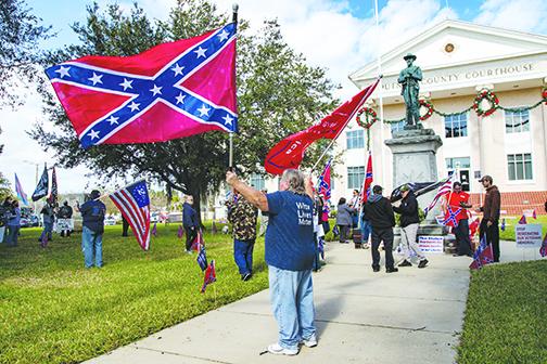 A protester wearing a White lives matter shirt waves flags in support of the Confederacy and President Donald Trump during the protest.