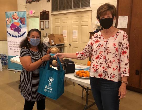 Baby Brain Builders President Angela Mills, right, gives one of the organization’s bags to a local resident recently. The nonprofit organization encourages parents and caregivers to talk to their babies and sound out words.