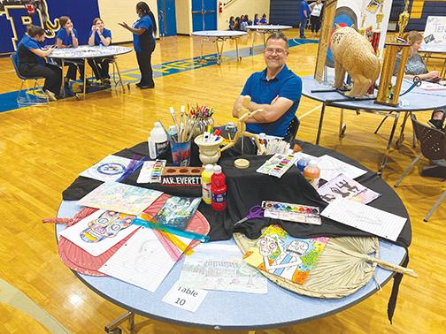 Palatka High School art teacher Michael Everett sits at a table displaying samples of work prospective students could be creating in his class. Everett was one of the teachers who participated in the school’s orientation for students who will begin attending the school during the next academic year.