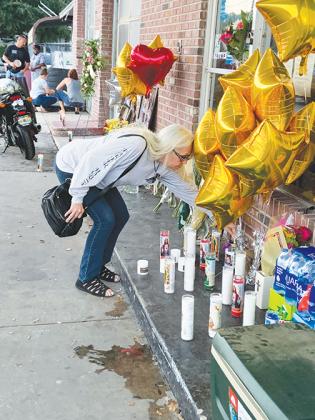 A woman places a candle among tributes left for Mark Anthony Arbelo Jr. before a vigil service held at M.A.Rims & Tires on Friday night in Crescent City.