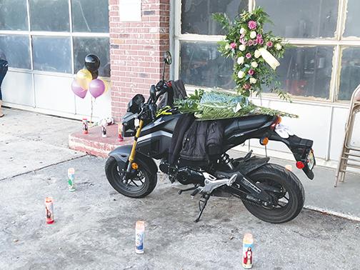 Tributes surround Mark Anthony Arbelo Jr.’s motorcycle before a vigil service Friday night at his father’s business in Crescent City.