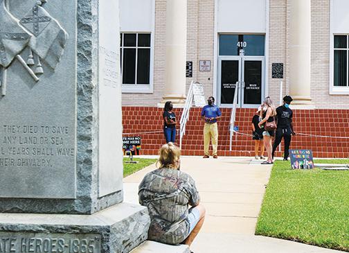 Stand Your Ground Putnam County representative Sheila Beck sits on the edge of the Confederate monument at the Putnam County Courthouse on Monday as members of the Putnam Alliance for Equity and Justice pray in front of the courthouse.
