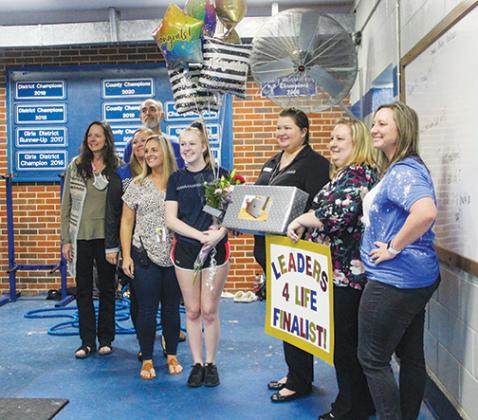 Interlachen Junior-Senior High School senior Sidney Williams smiles with her mom and school district officials after they surprised her during a weightlifting practice on Wednesday to tell her she was moving to the next round in her bid to be a Leader 4 Life.