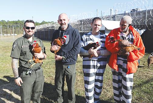 Putnam County Sheriff’s Office Jail Director Maj. Scott Surrency, Deputy Brian Smith and two inmates hold the agency’s chickens Tuesday so the animals’ Santa hats stay put.