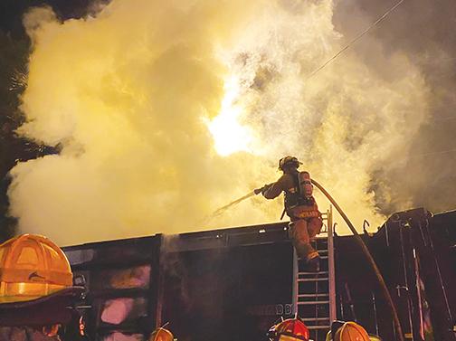 A firefighter stands atop a ladder as he attempts to put out the blaze that erupted in a Palatka garbage truck.