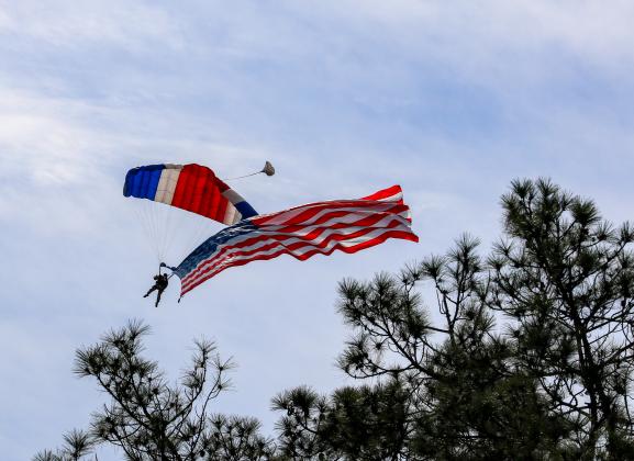 An American flag waves in the sky behind a parachuter at the 11th Annual Fly-in and Classic Car Show on Saturday. 