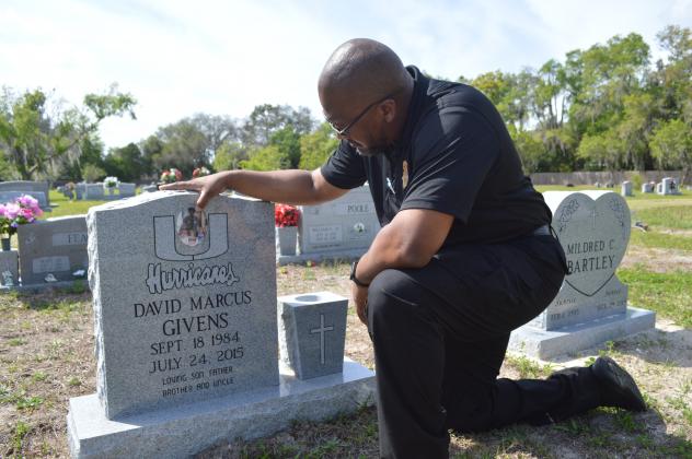 Casmira Harrison/Palatka Daily News Anterio Smith rubs some dirt off a photo of his little brother and his brother’s children that adorns David Marcus Givens’ grave. Smith, who works in the medical examiner's office that oversees Putnam County deaths, wants his brother’s killers brought to justice and to see fewer familiar faces in the morgue.