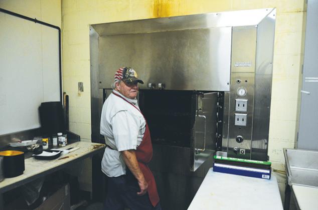Meat Cutter Paul Seay stands beside a smoker full of cooking meats at the store.