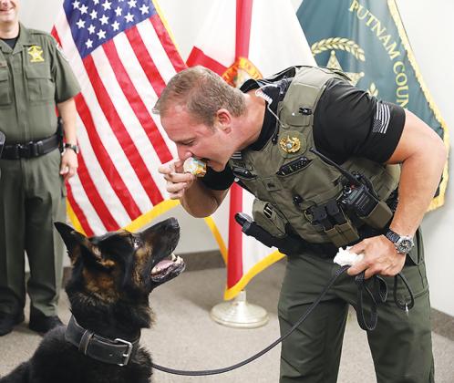 Putnam County Sheriff’s Office Lt. Jared Guy takes a bite of K-9 Halo’s treats during the dog’s retirement party on Monday.