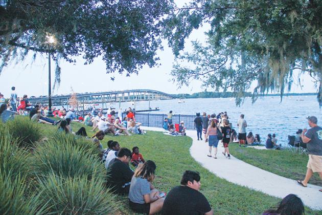 People sit along the Palatka riverfront Monday evening as they wait for nightfall so they can watch the city’s fireworks display over the St. Johns River.