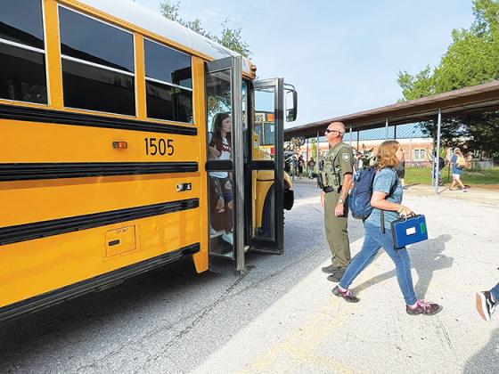 A law enforcement officer helps Putnam County high-schoolers get off the bus on the first day of school.