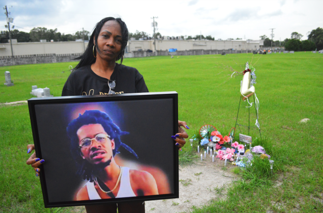 Martha Kearse holds a photo of her son, Shiron Brooks, at his graveside in Oak Hill West Cemetery in Palatka on Thursday, August 18, 2022. Brooks was killed in May. A candlelight vigil for him will be held Saturday at Booker Park. 