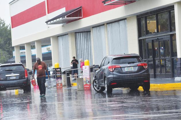 A shopper carries groceries through the rain at the Palatka Winn-Dixie on Wednesday afternoon before the grocery store closed.
