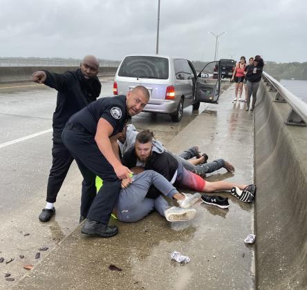 Civilians and an officer from the Palatka Police Department hold down a man who authorities said was sitting on the railing of the Memorial Bridge on Thursday morning holding a knife.