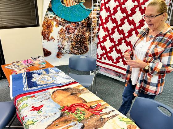 Darlene Walker talks about the intricate beadwork she did on some Christmas panels that are being featured at the quilt show that runs through noon Saturday at the Palatka Headquarters Library. (SARAH CAVACINI/ Palatka Daily News) 