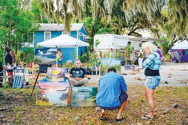 File photo. Two people look over a vendor's art as they determine whether to make a purchase at the Crescent City Art & Farmers Market last summer.