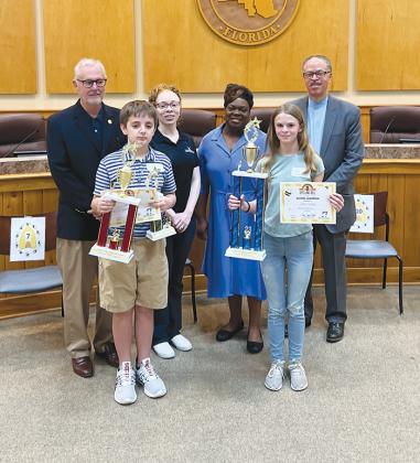 Spelling bee champion Jillian Huntley, front right, and runner-up Nicolas Penta, front left, hold their trophies and certificates after the 54th Annual Putnam County School District Spelling Bee on Wednesday. They are standing with the Flagg family, who provided the trophies, and Joe Pickens, the spelling bee moderator and president of St. Johns River State College.