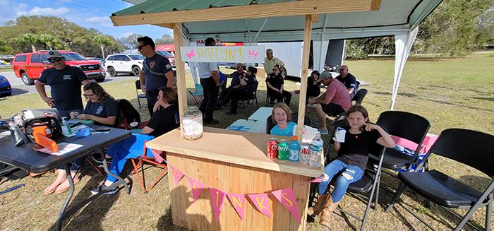Eight-year-old Raegan Gill, right, and 7-year-old Paityn Wilkinson, seated beside her, work a lemonade stand Friday at the Putnam County Government Complex. The two girls were helping first responders with the Putnam County Fire Rescue Local 3529 firefighters union raise money for 5-year-old Nathan Scott. Nathan was severely injured in an accidental fire at his West Putnam home Christmas Eve.