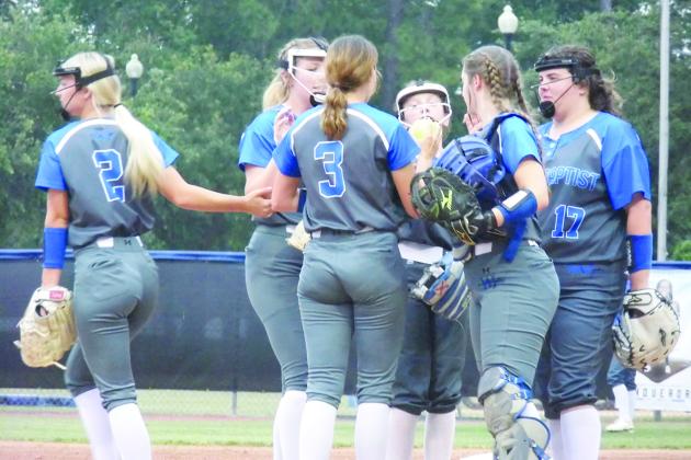 Peniel Baptist Academy softball players gather around pitcher Alexis Wallace (3) after host Jacksonville Trinity Chrisian scored four runs in the second inning in the Region 1-2A tournament opener Wednesday night. (COREY DAVIS / Palatka Daily News)
