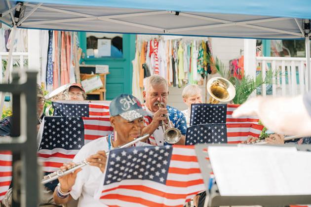 Members of a community band play music they are reading from music stands painted to look like American flags.